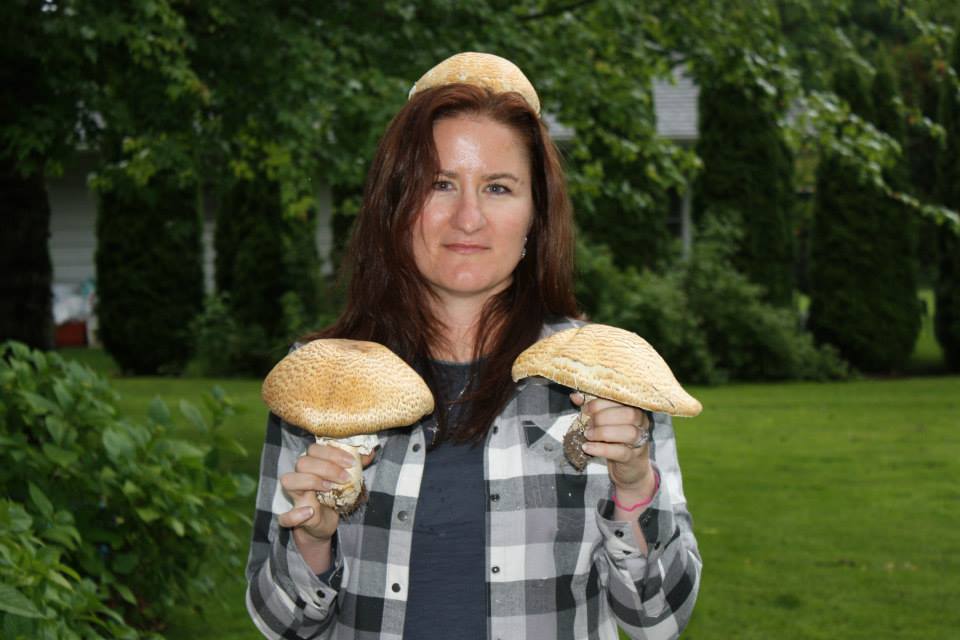 A forager holding up two king bolete mushrooms, with a third balanced on her head