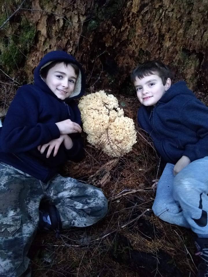 Two kids kneeling next to a lion's mane mushroom find in the forest