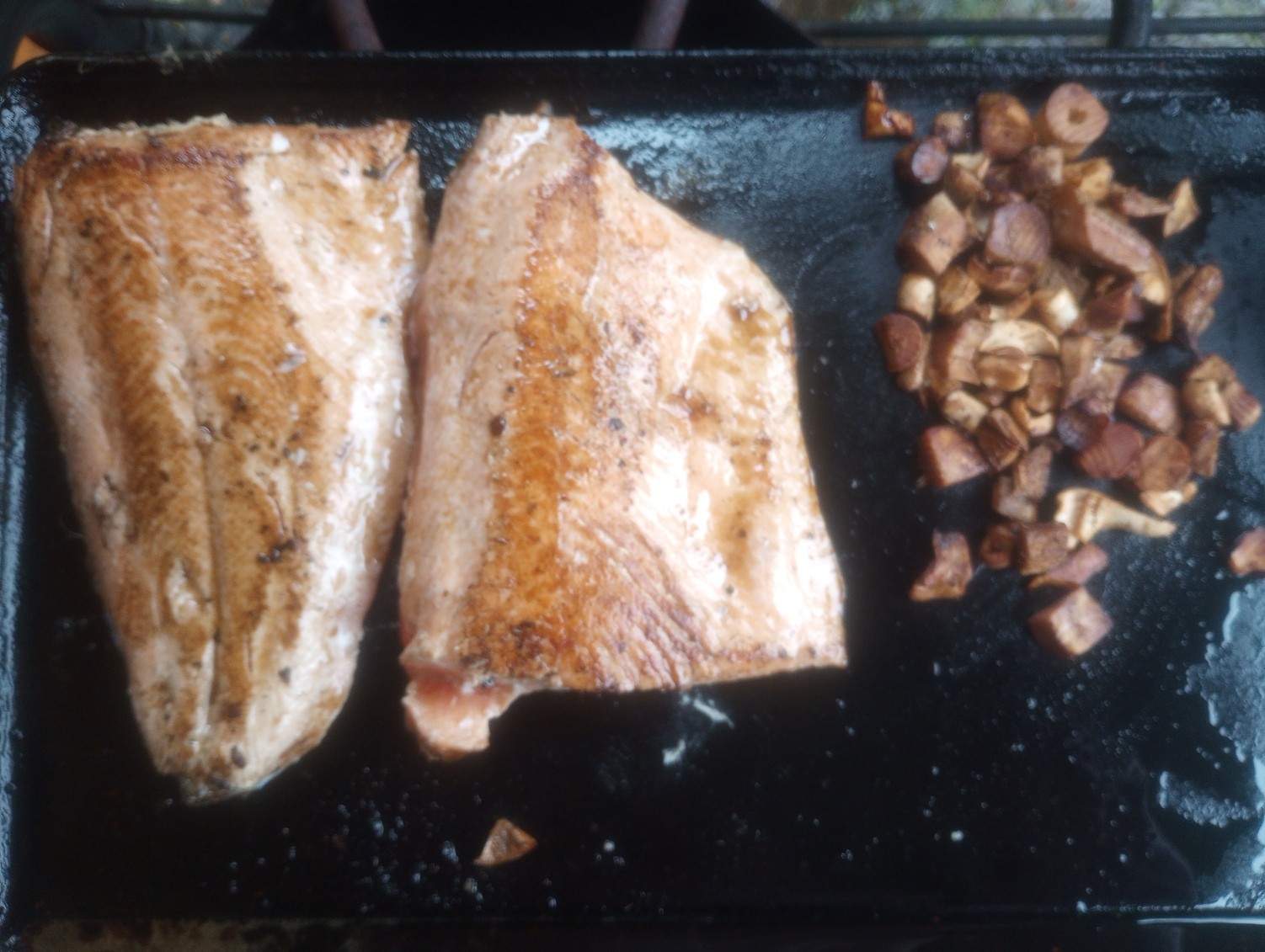 Fish fillets and diced wild mushrooms cooking together on a griddle